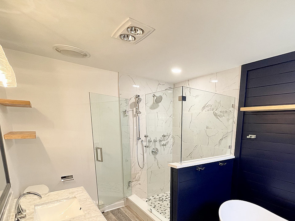 Remodeled bathroom with a navy shiplap wall, glass shower and freestanding tub