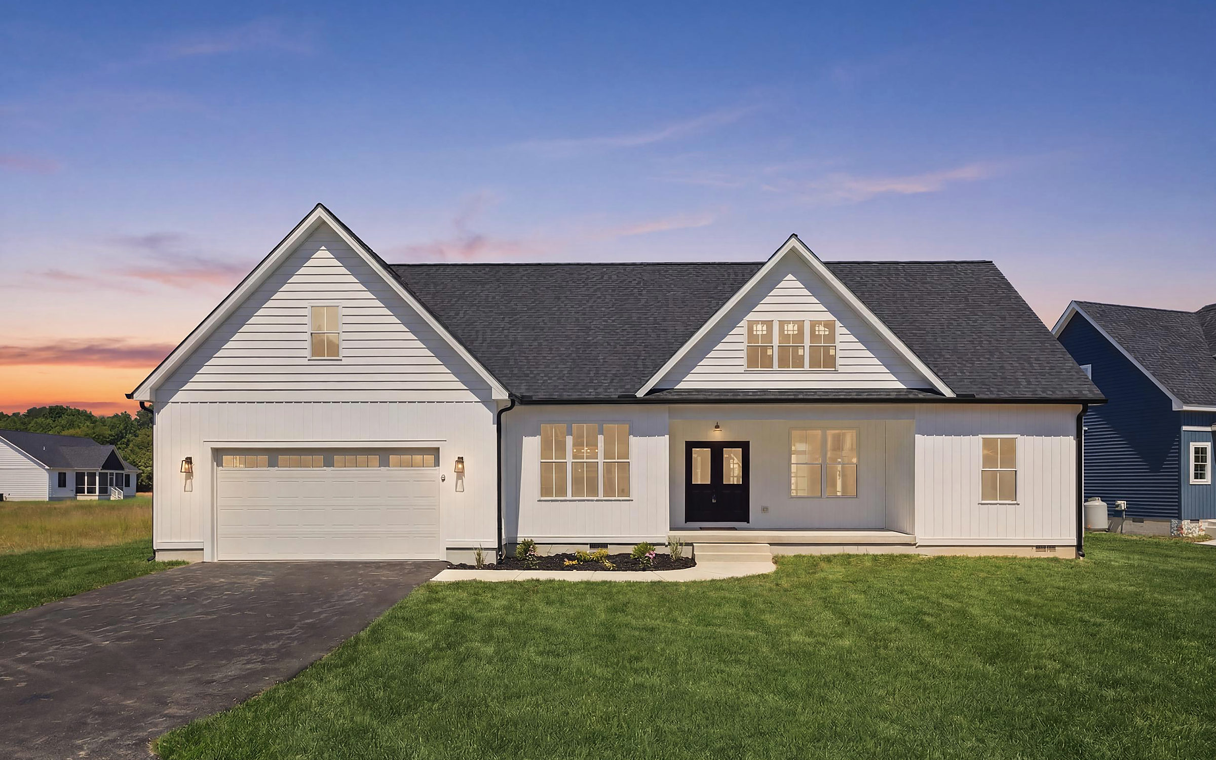 A white Del Mar custom home with a two-car garage at dusk in Berlin, Maryland