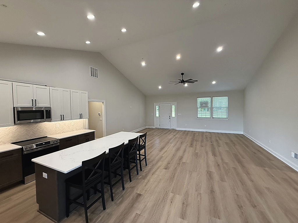 A Del Mar kitchen: white and dark wood cabinets, a long quartz island with seating and an open great room