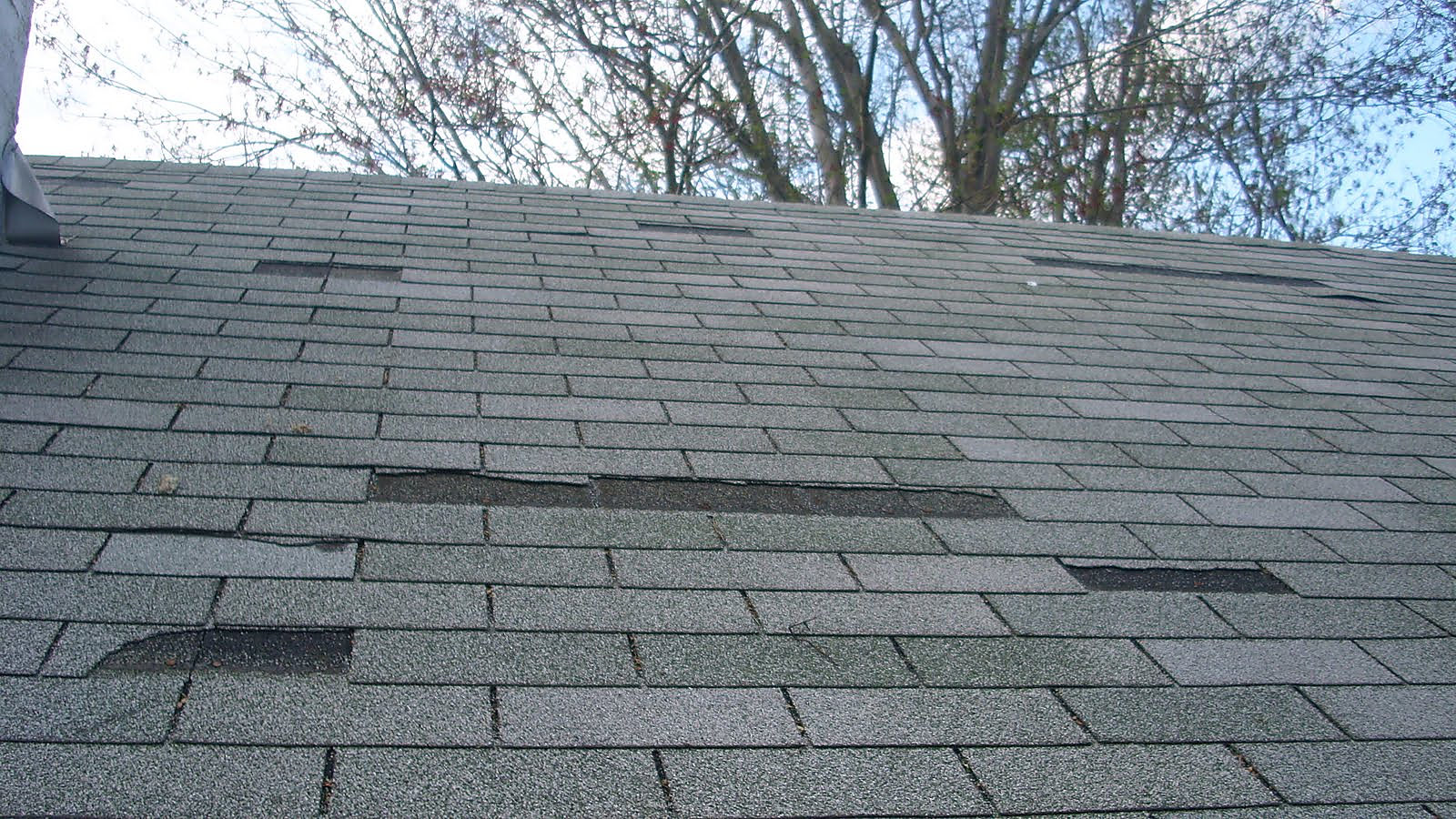 Missing and damaged shingles on a roof after a wind storm